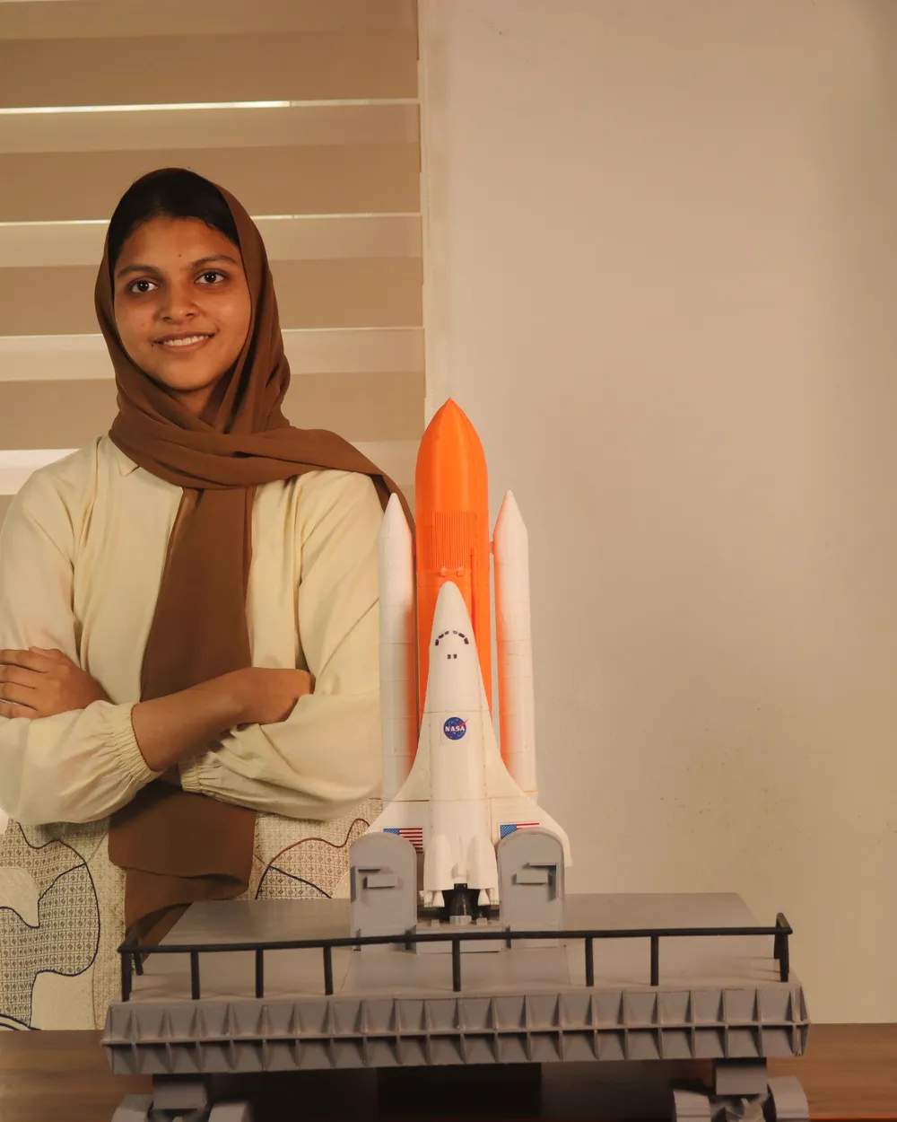 A student standing confidently beside a space shuttle model on its launch platform