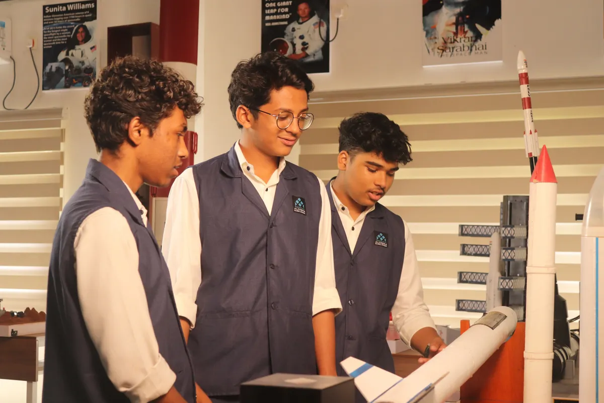Three students smiling as they hold a model rocket they built