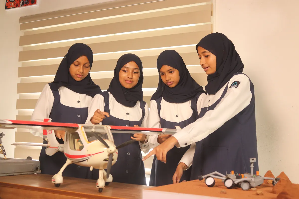 Students pointing out the control surfaces on a model aircraft